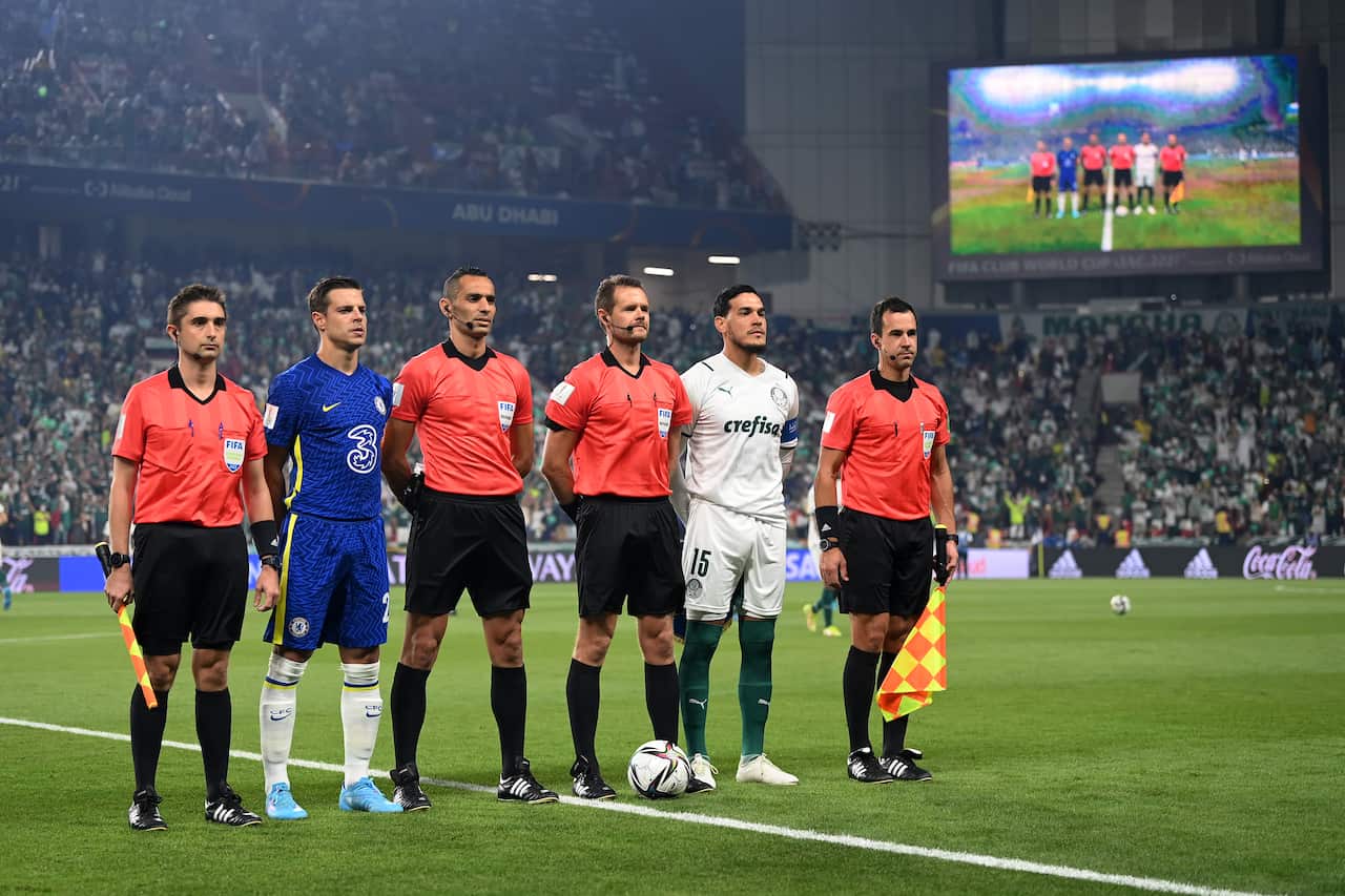 Referees and assistant referees standing in a line with footballers on the pitch