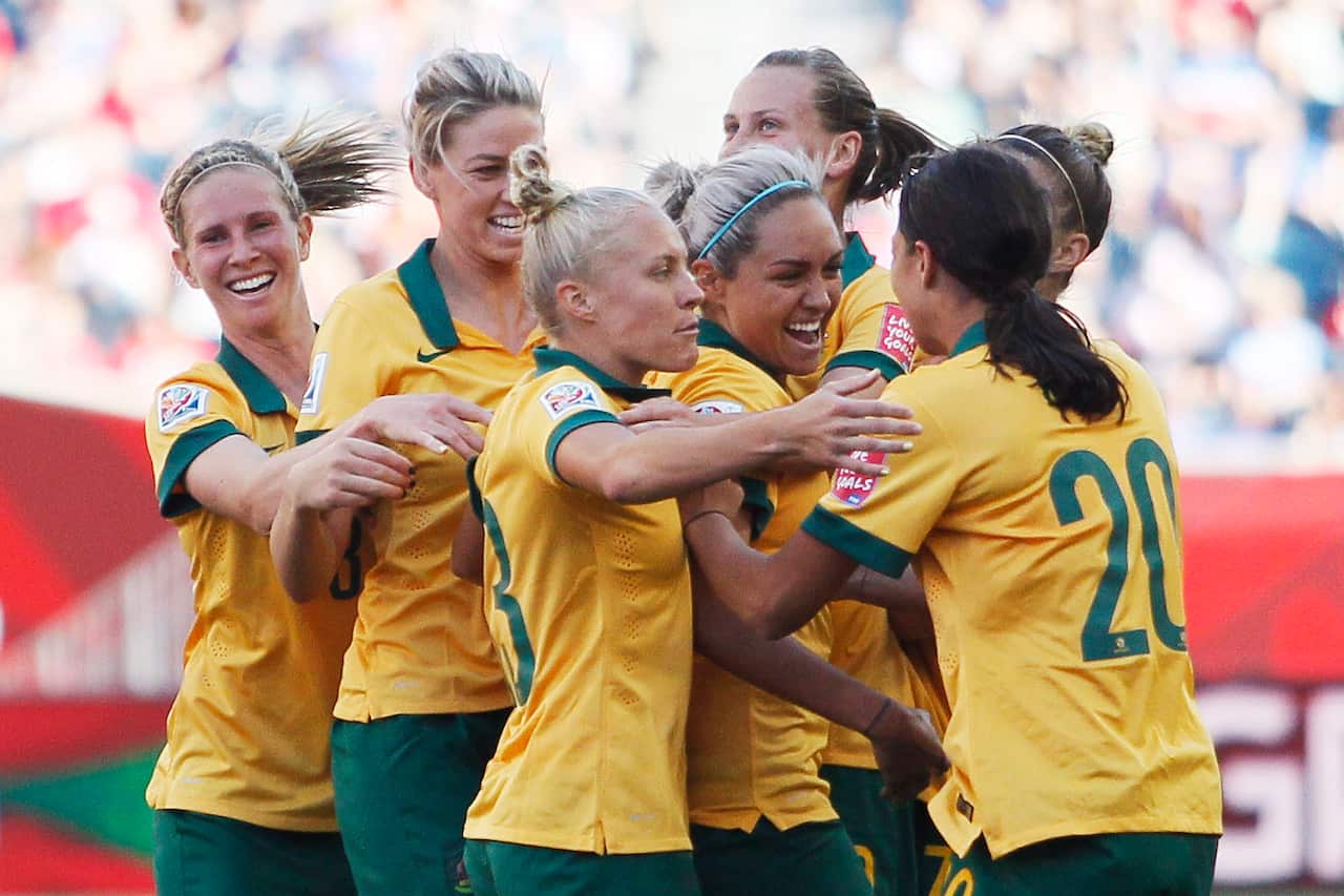 Matildas players in gold shirts and green shorts celebrate a goal