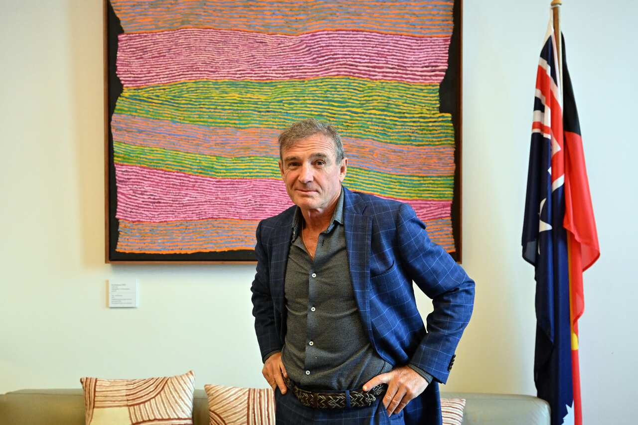 Man stands in front of flags and Indigenous art.