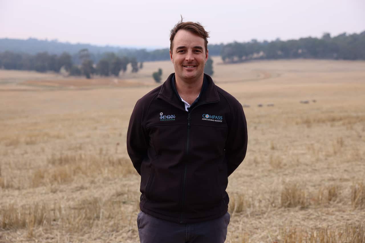 A male farmer looking at the camera with a rural farm in the background.