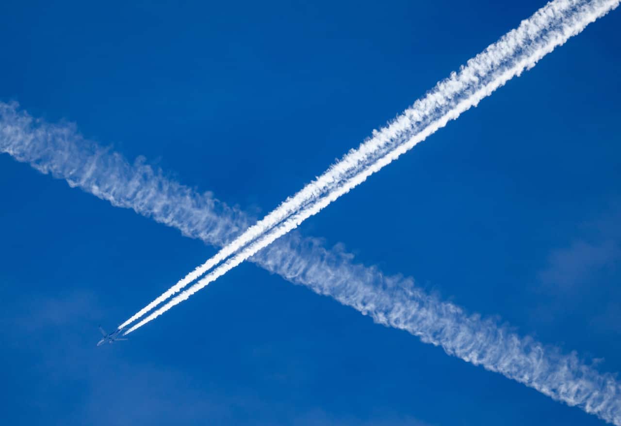 Two aeroplanes travelling through the sky, both with condensation trails behind them.
