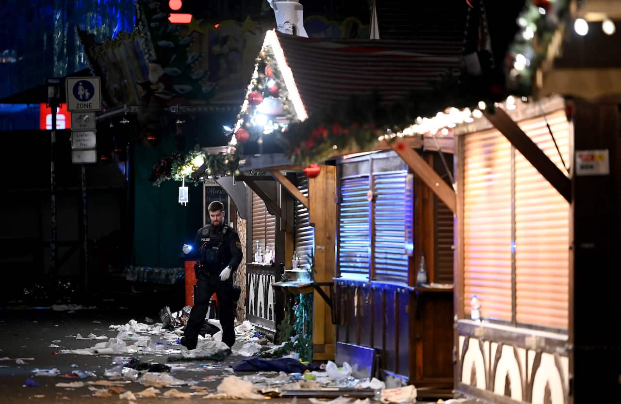 A police officer walks near Christmas market stalls that have their windows shut. Debris is strewn across the ground.