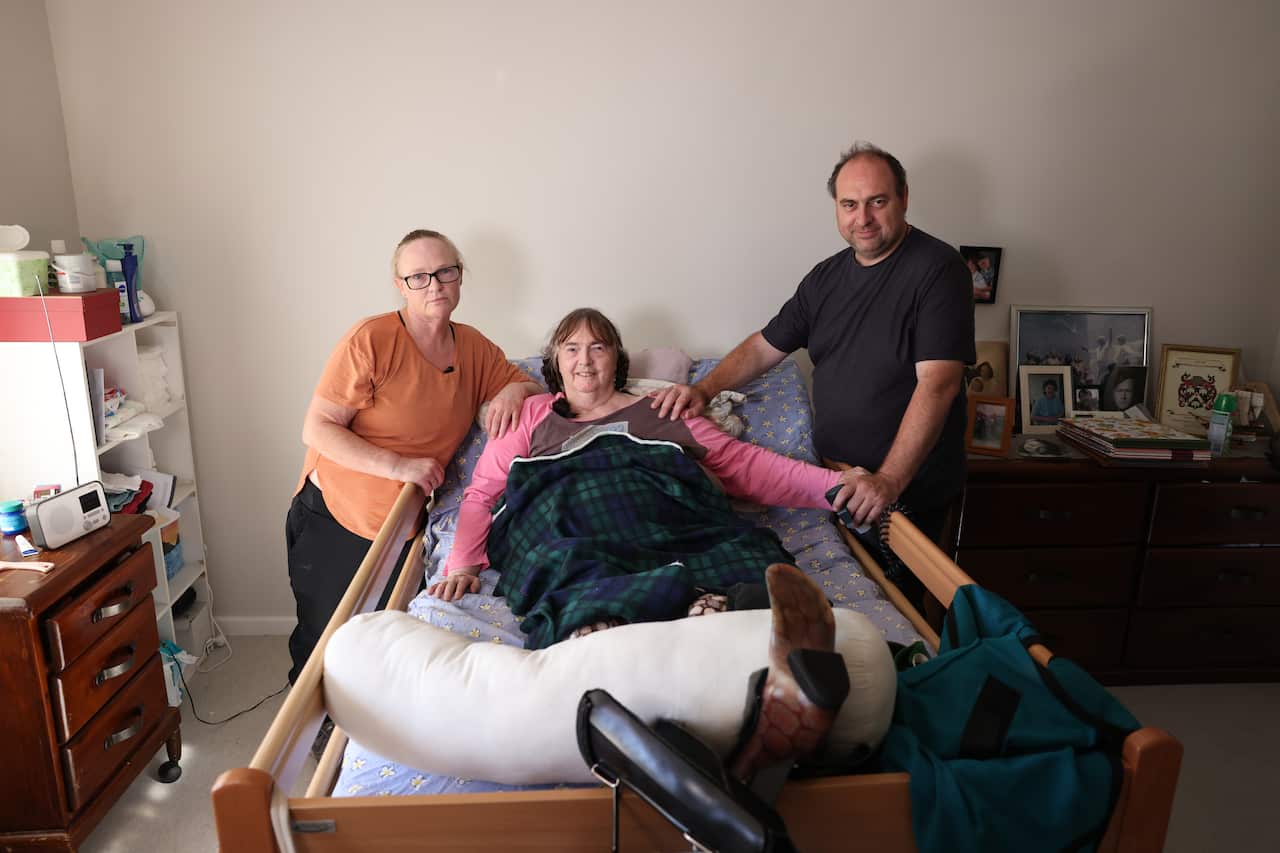 An older woman laying in bed with a younger man and woman on either side of her.