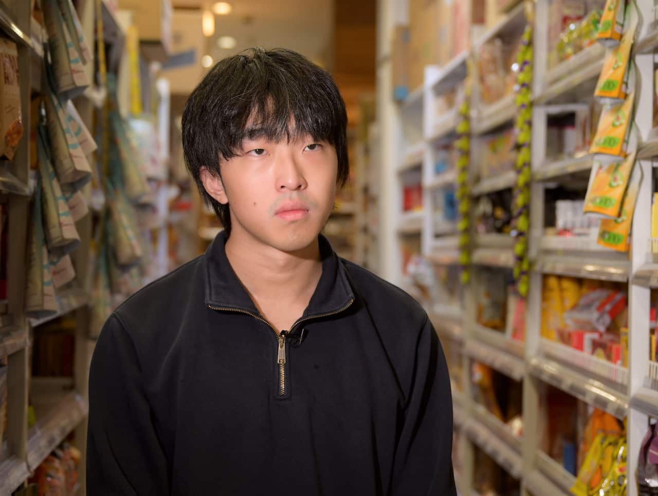 A man wearing a black jumper sits in a supermarket aisle.