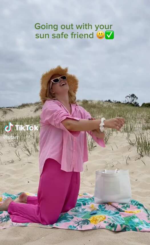 Woman wearing pink clothing applies sunscreen at the beach.