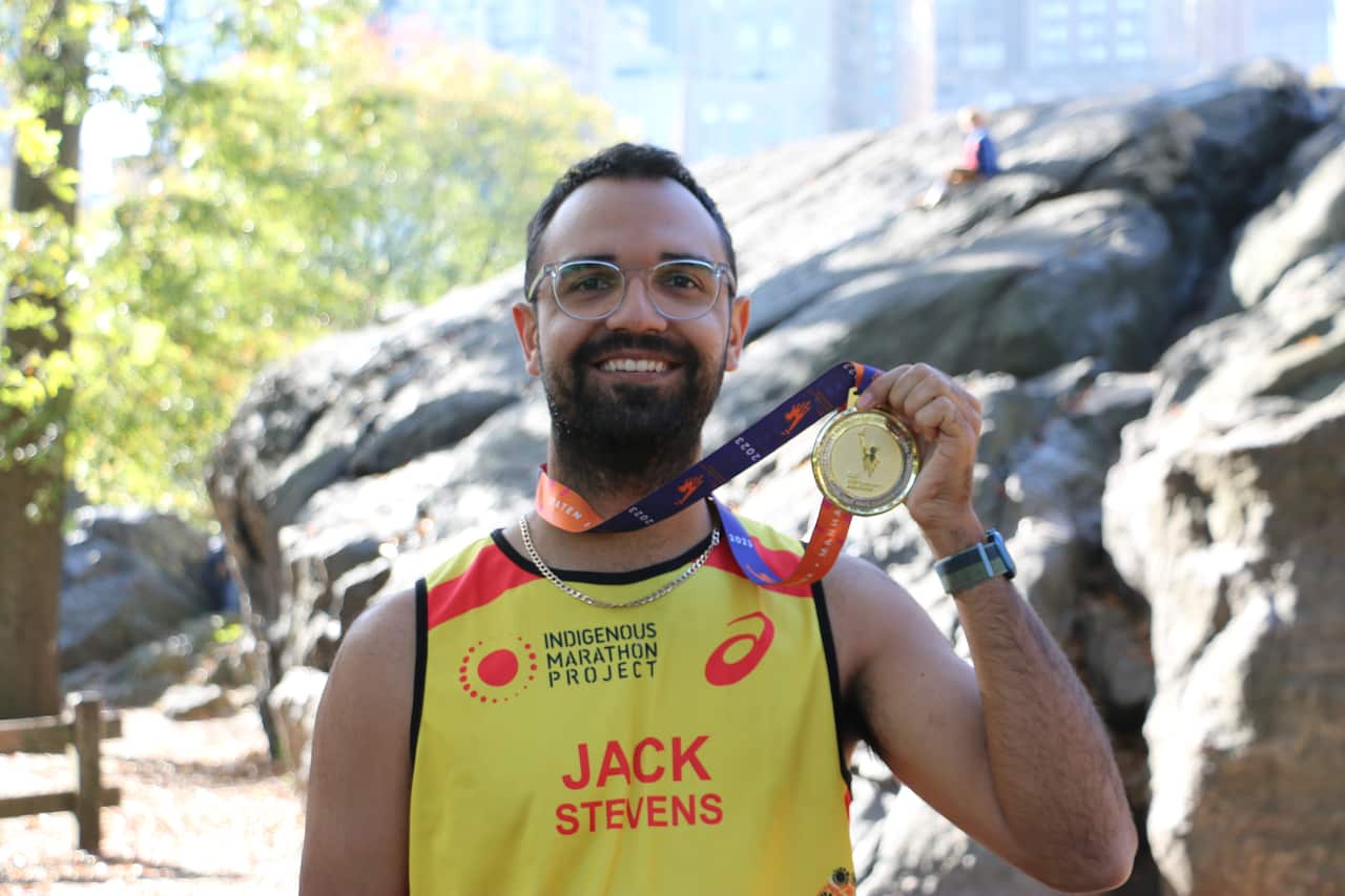 Proud Gunggandji man, Jack Stevens smiles after completing the New York City Marathon in 2023. He holds up a medal on his neck.