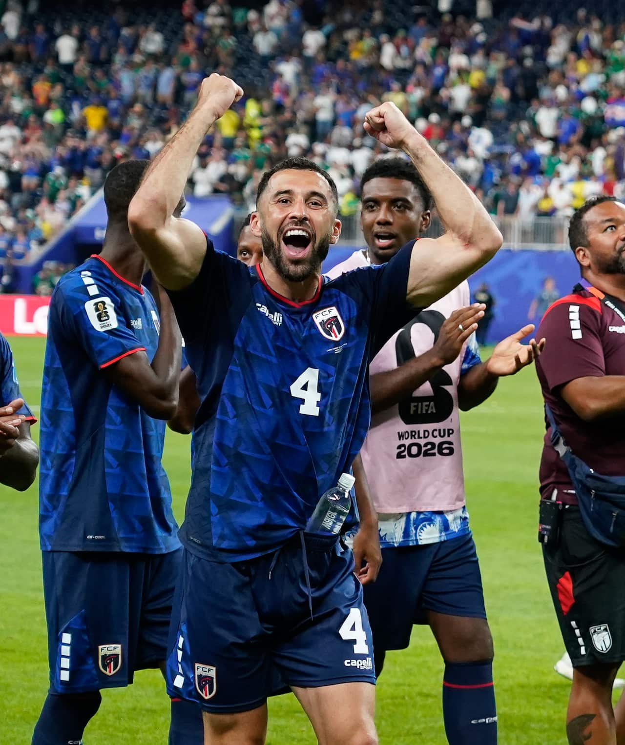 Pico Lopes celebrates a draw wearing a blue shirt with his arms up in the air while team mates celebrate behind him