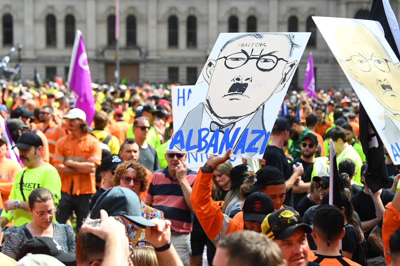 Tradies in fluro gear, protesting. One holds up a sign that says Alba Nazi with a cartoon picture of the prime minister.