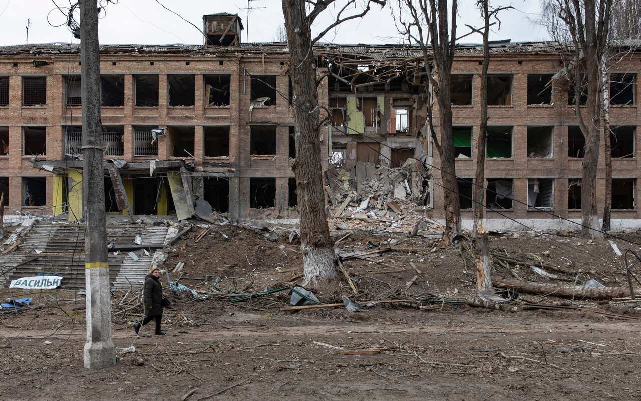 An individual is seen walking past a destroyed building.