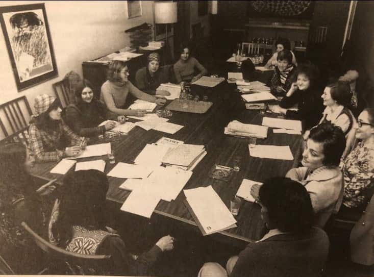 a black and white photo of women sitting around a table