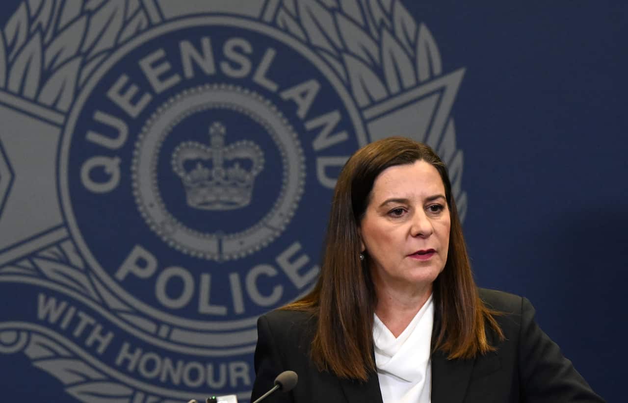 A middle-aged white woman wearing a suit jacket speaks at a lectern. A sign displaying the Queensland police insignia displayed behind her.