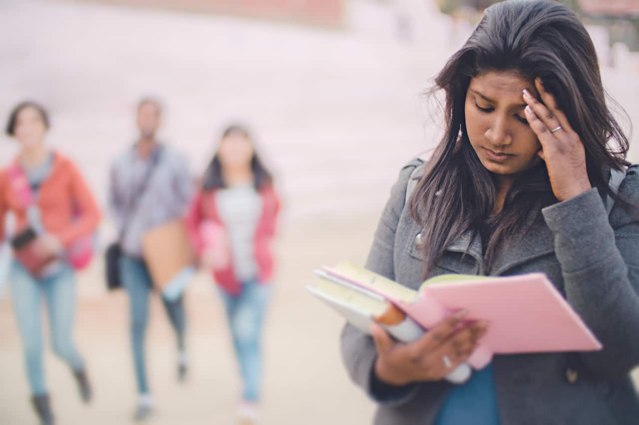 Sad female college student holding her head and reading book.