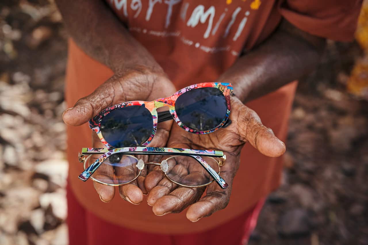 A close up of open palms holding a pair of sunglasses and spectacles with Helen's distinctive colourful designs adorning the arms. 