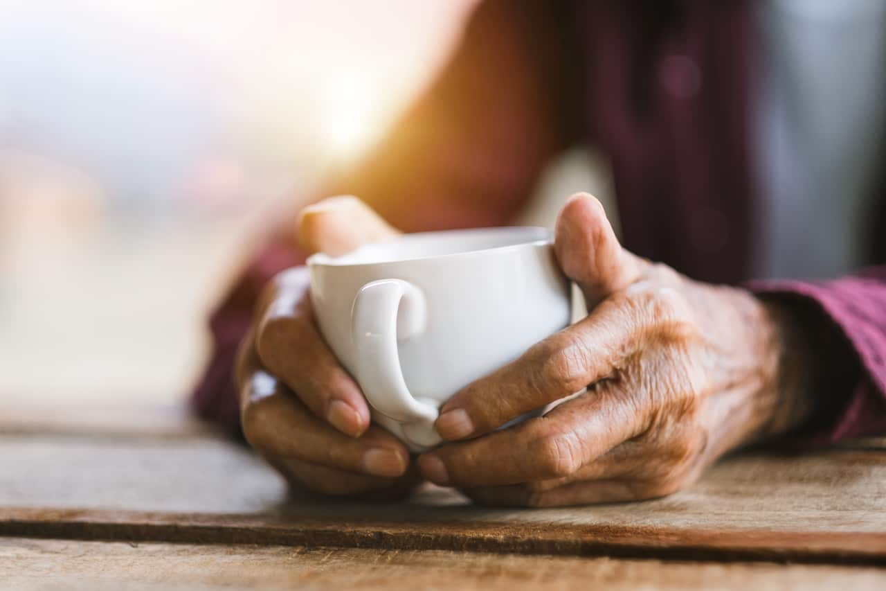 Hands of old man holding cup of coffee on the wood table.vintage tone