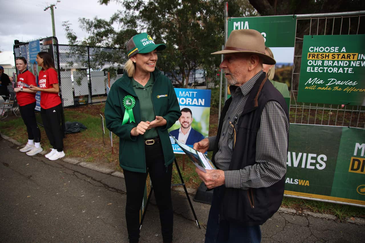 A woman in green National Party attire speaks to an older man in an Akubra-style hat.