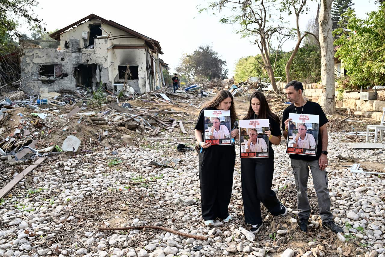 Family members of hostages taken by Hamas stand in the rubble of a kibbutz.