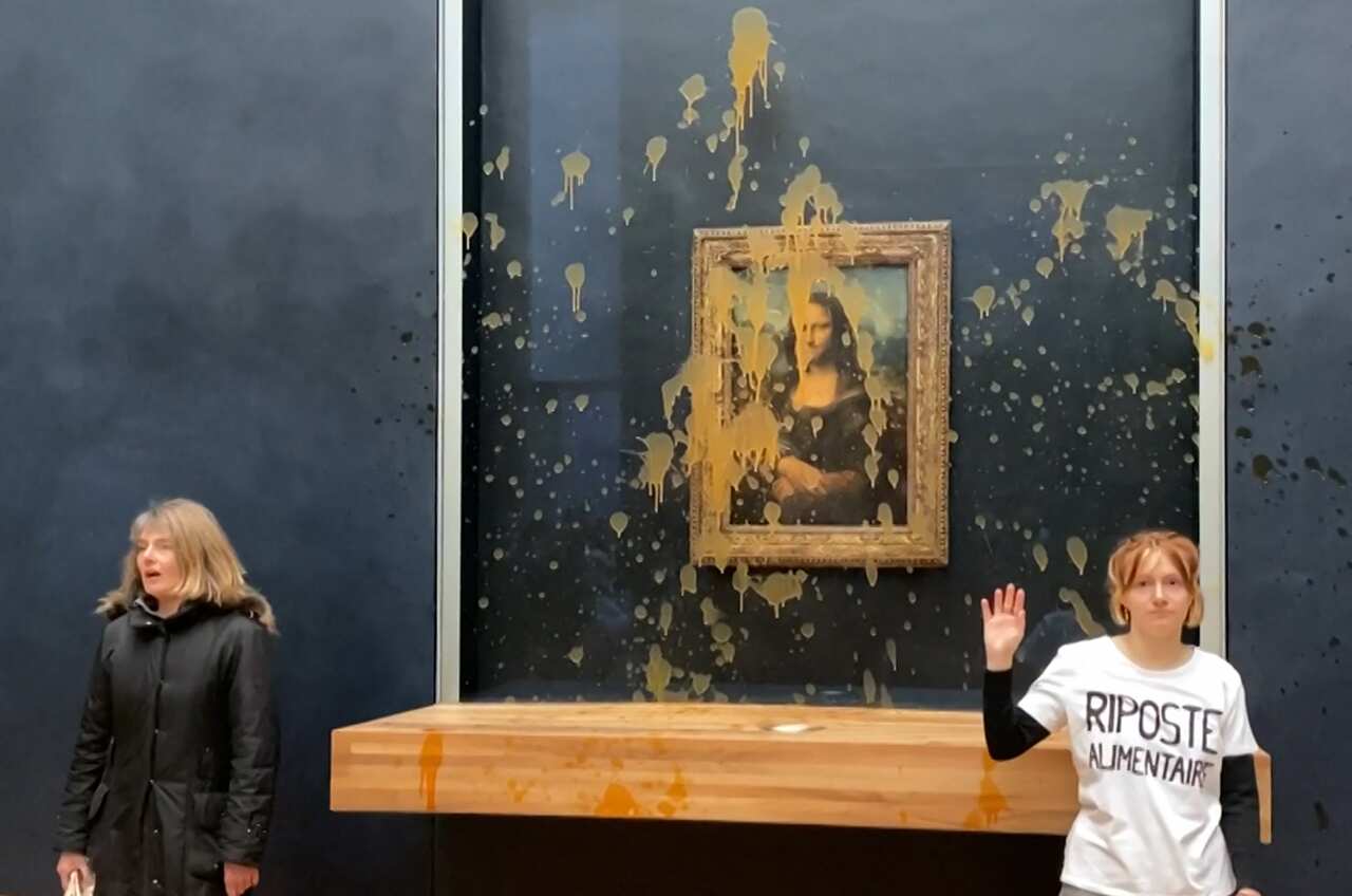 Two environmental activists from the collective dubbed Riposte Alimentaire (Food Retaliation) gesturing as they stand in front of Leonardo Da Vinci's Mona Lisa.