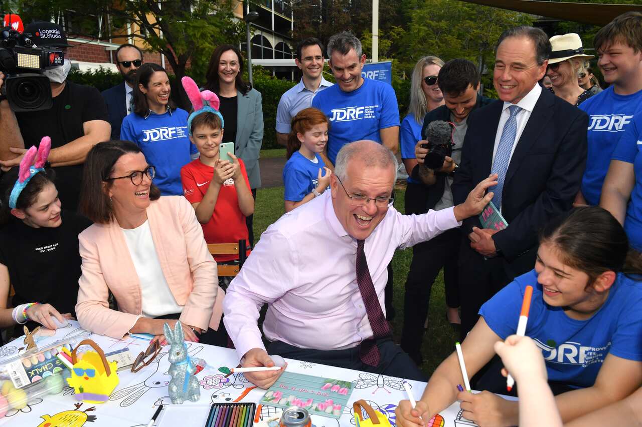 Scott Morrison sitting at a table with a group of people behind him.