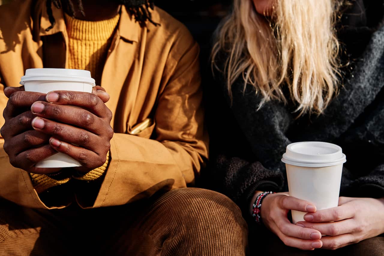 The hands of two people, each holding takeaway disposable coffee sups.
