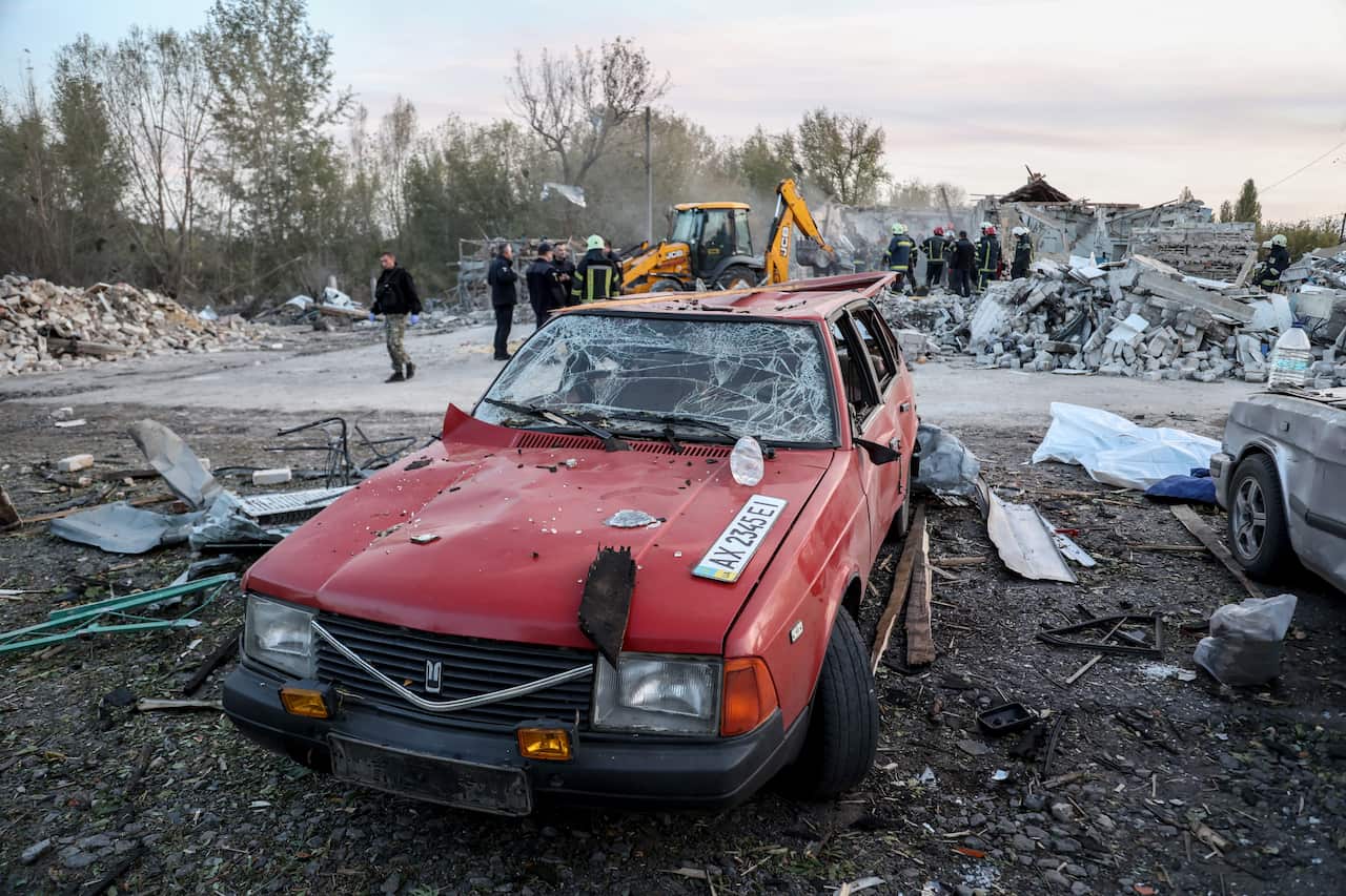 Red car with cracked window sits in dirt, surrounded by rubble.