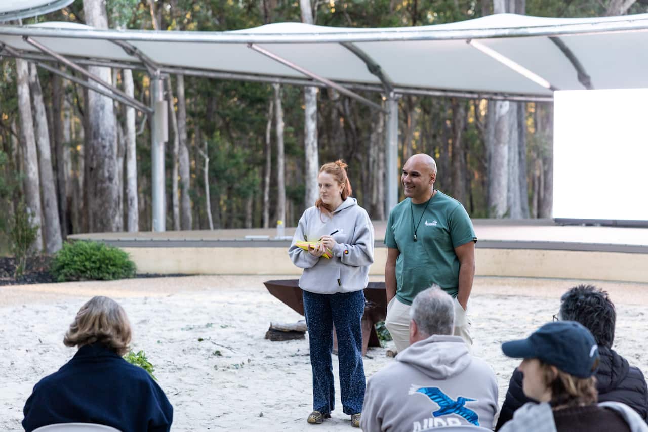A man and woman standing in front of a group of people watching on.