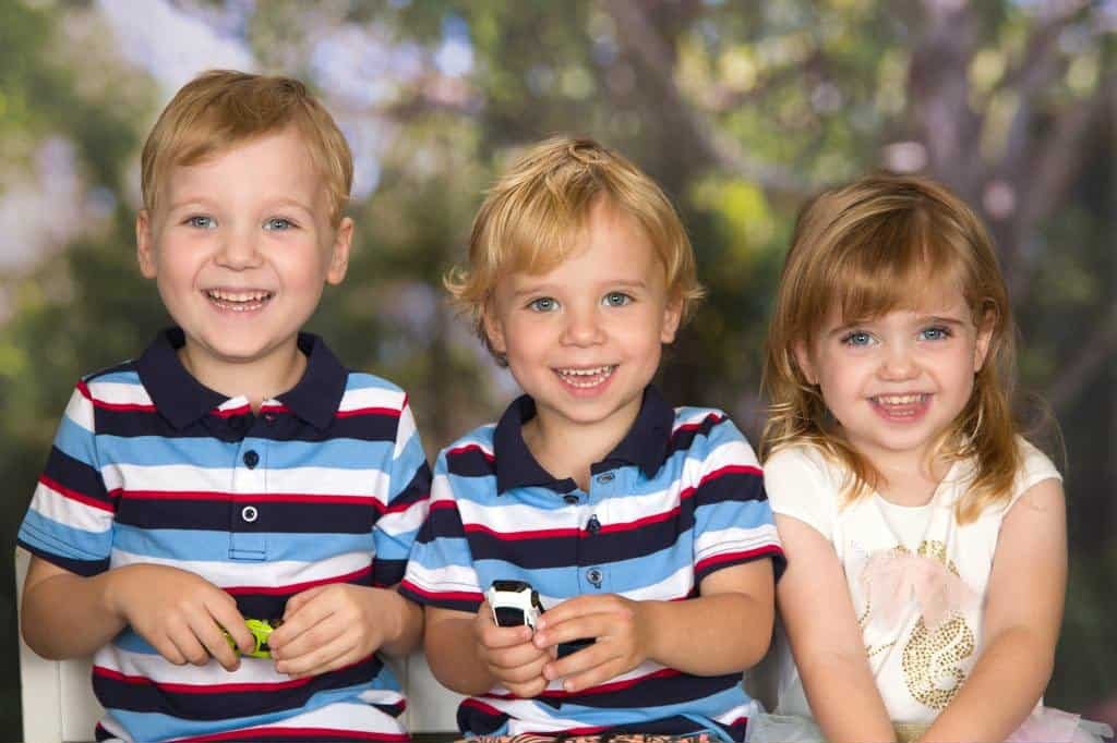 Three children, two boys in striped shirts and a young girl in a white top, all smiling.