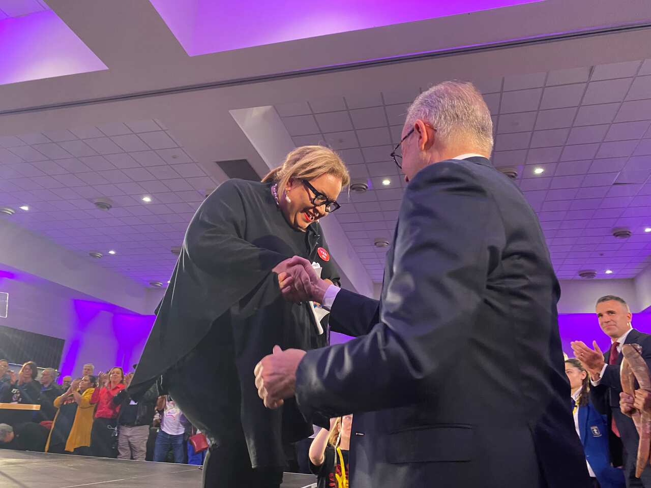 Woman smiles as the is helped off stage by a man.