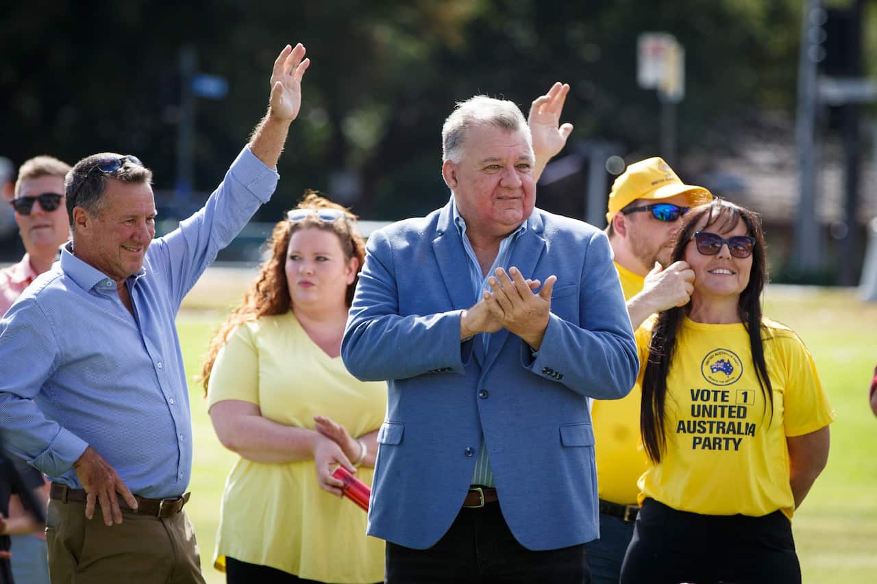 Craig Kelly standing and clapping. Four supporters are standing behind him.