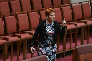 Pauline Hanson, wearing a floral dress, gesticulating in a room with red seats and pink carpet.