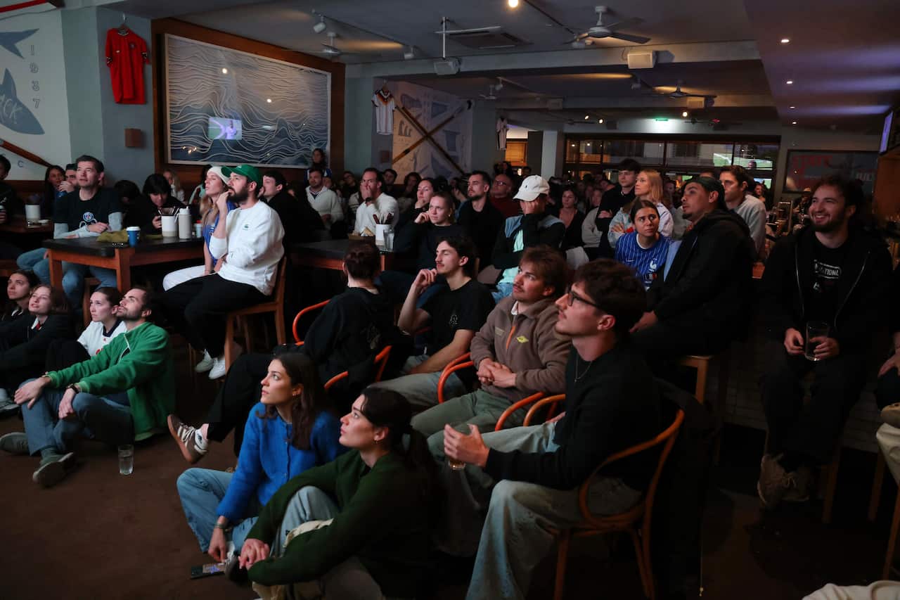 Football fans sit around en masse in a dark pub.