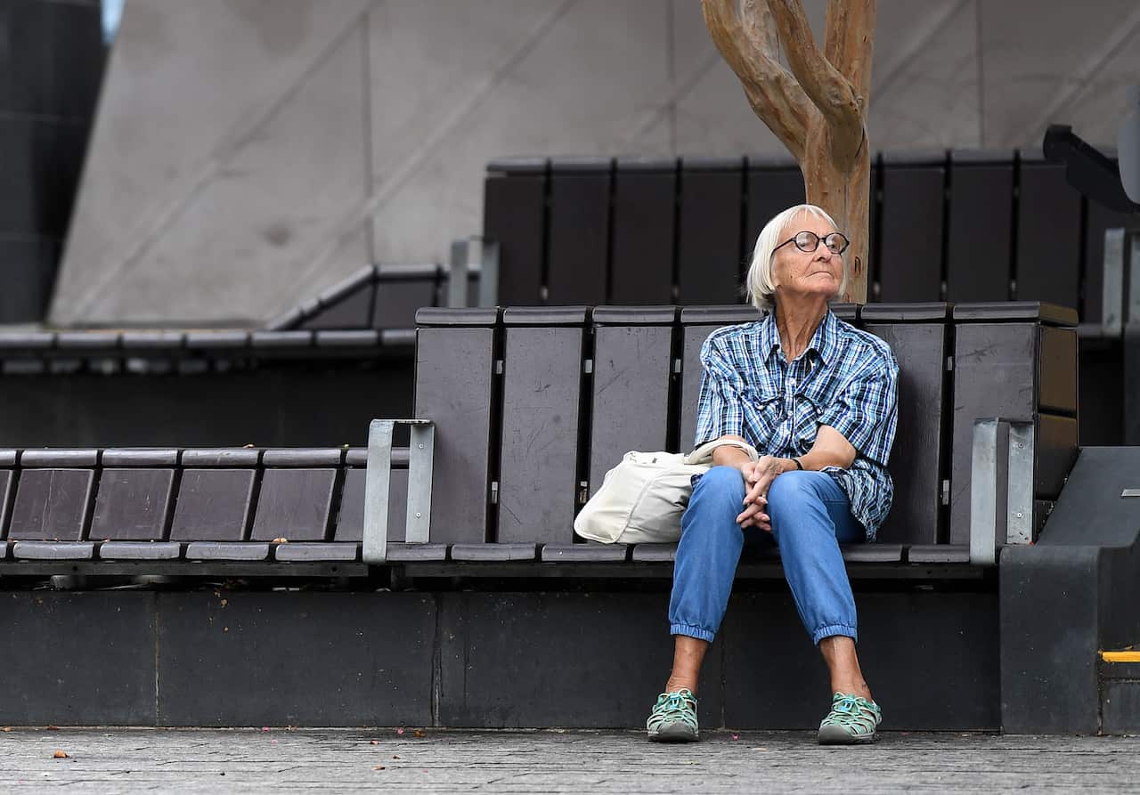 An elderly woman sits on a bench.