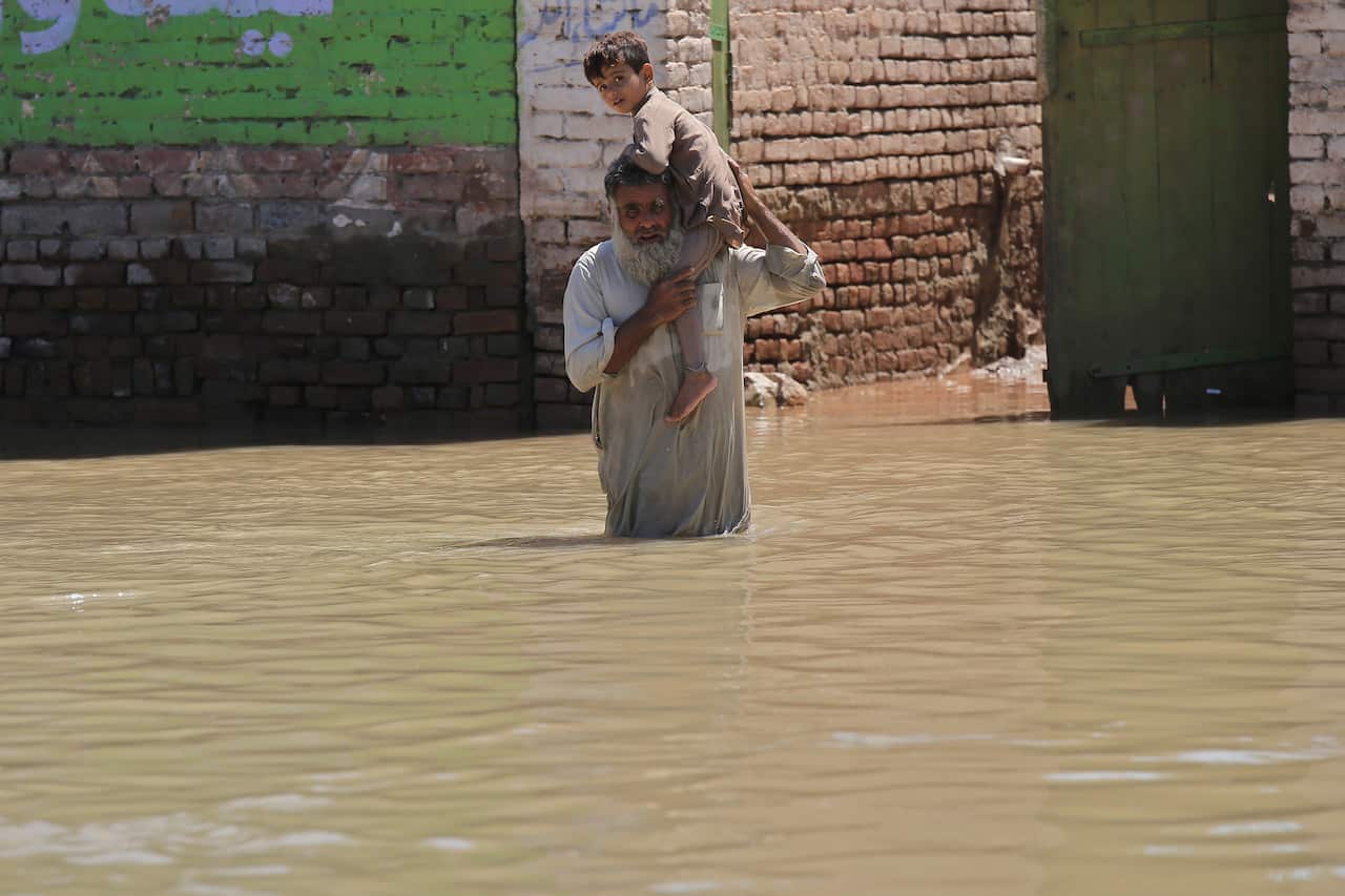  Man holding child wades through a flooded area