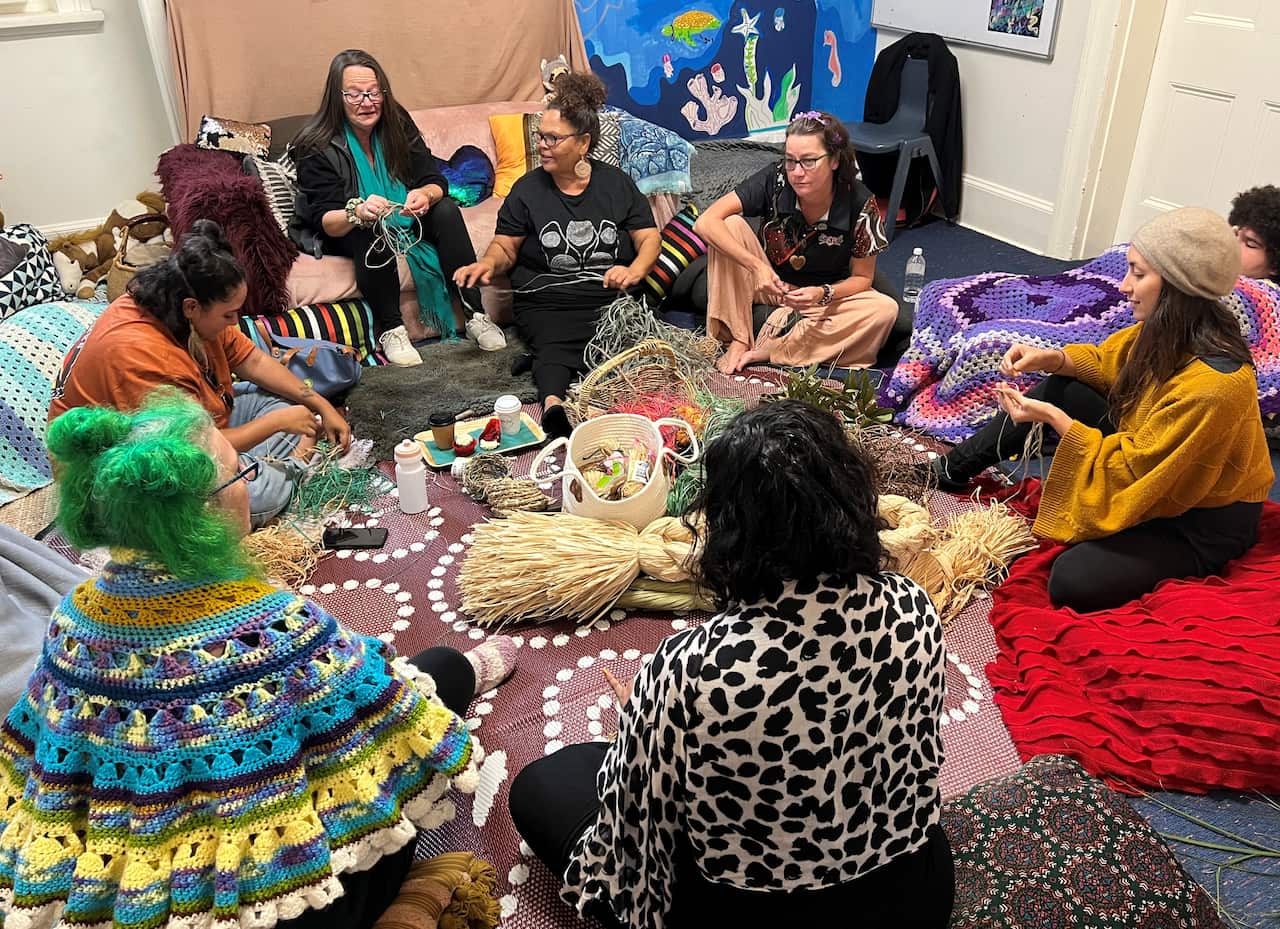 Indigenous women sit in a circle and weave
