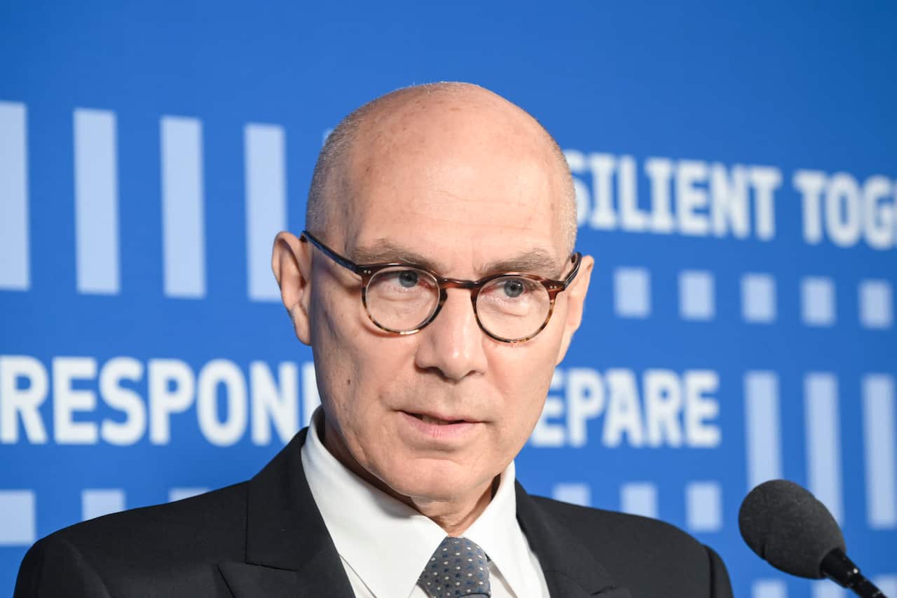 A man speaking into a microphone, with a blue background behind him.