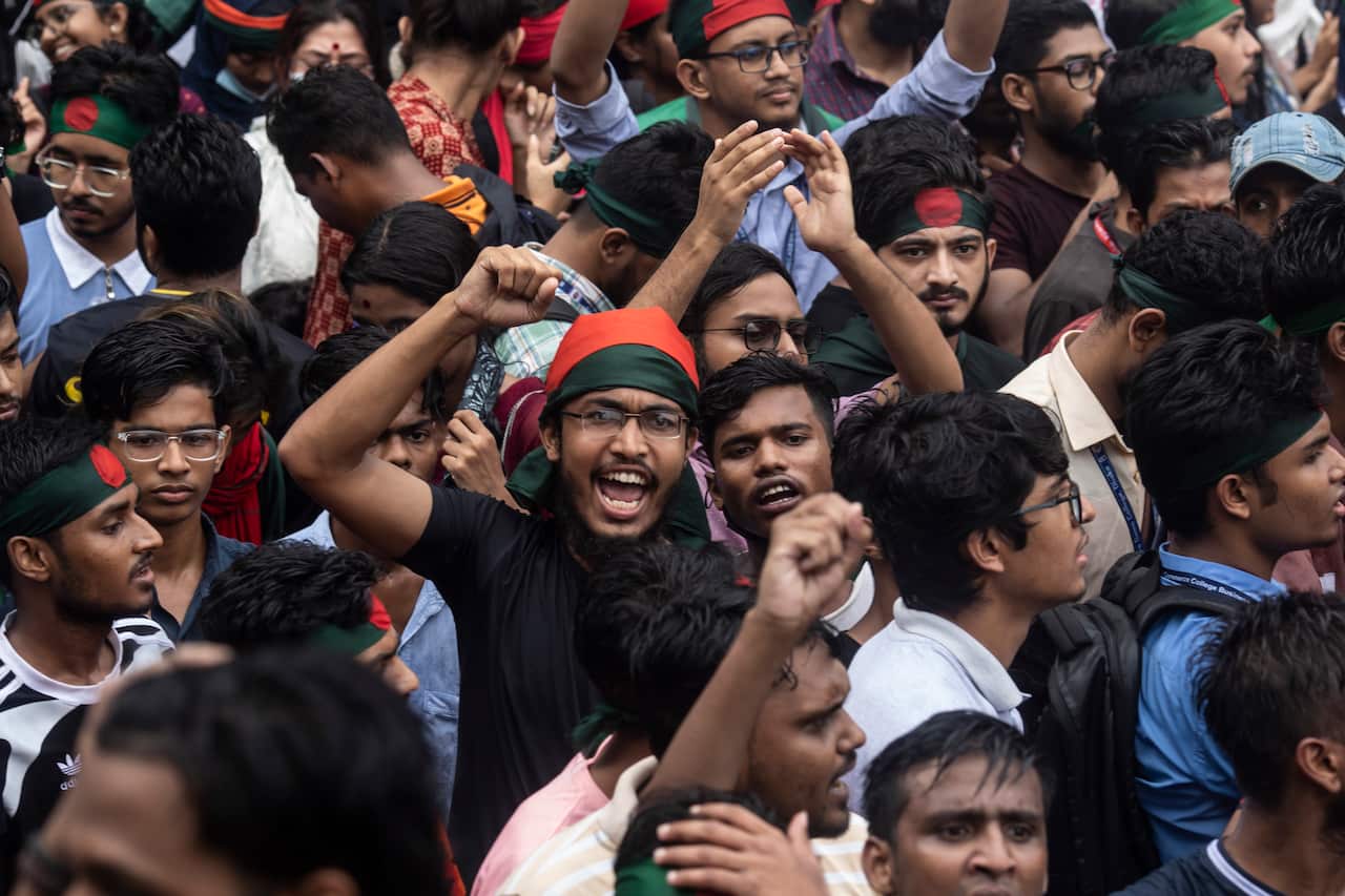 Protesters seen in Dhaka. Many are raising their fists and chanting. Many are wearing red and dark green headbands. 