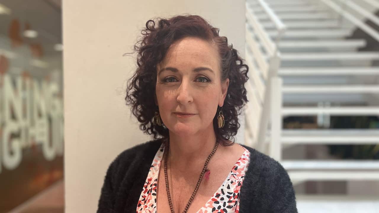 a middle aged woman with red curly hair stands in a white office