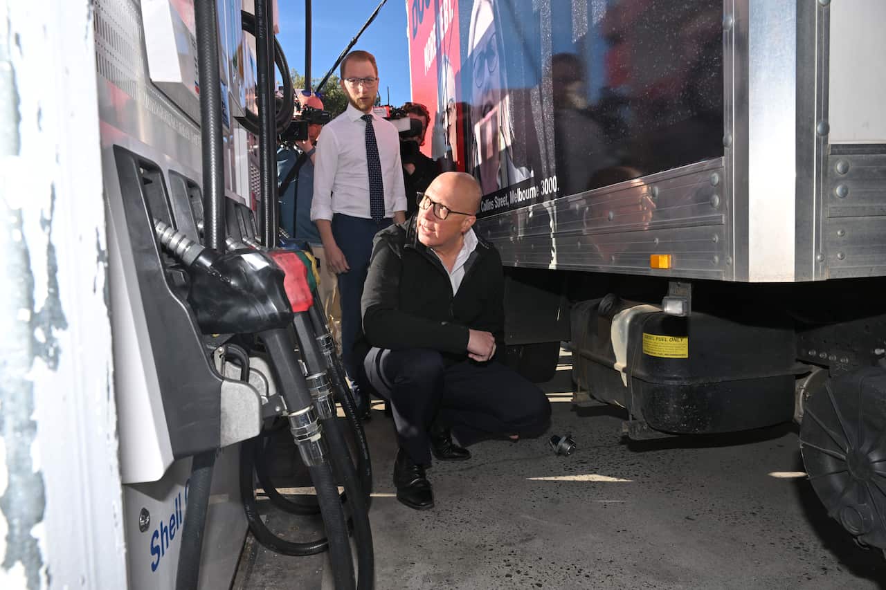 A man kneels next to a bowser and a truck at a petrol station.