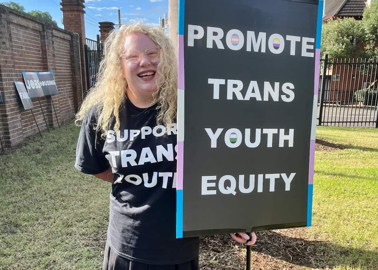 Mum and Executive Director of Parents for Transgender Youth Equity Lannen Stapleton holding a sign that says promote trans youth equity.