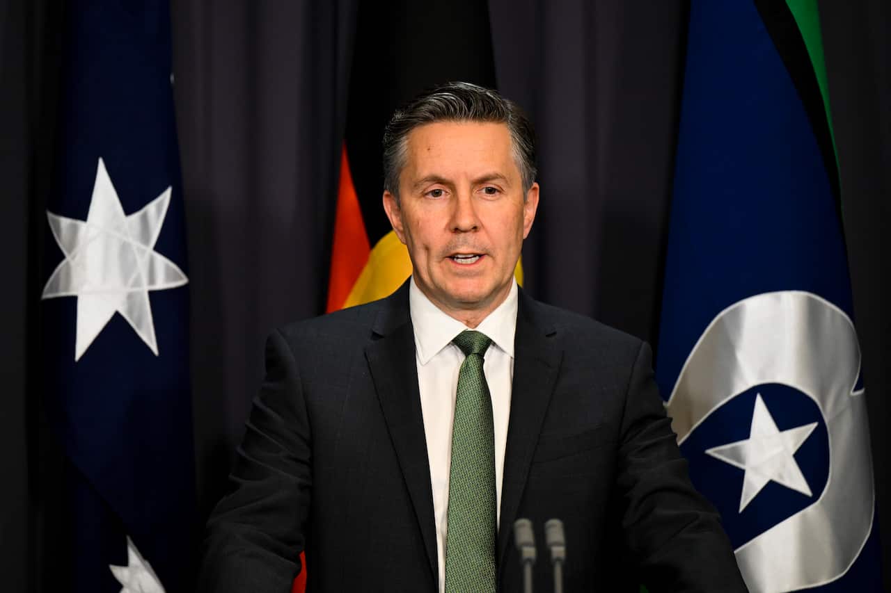 A man in a black suit speaks into microphones.