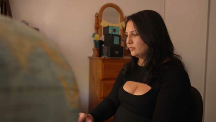 A woman wearing a black top sitting in a chair in a room. There is a globe in the foreground.