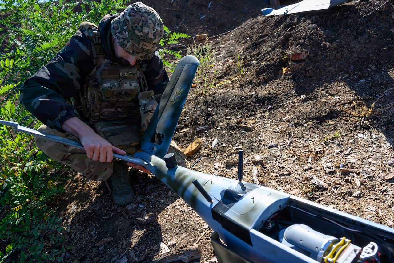 A soldier in camouflage works on assembling or repairing a military drone outdoors.