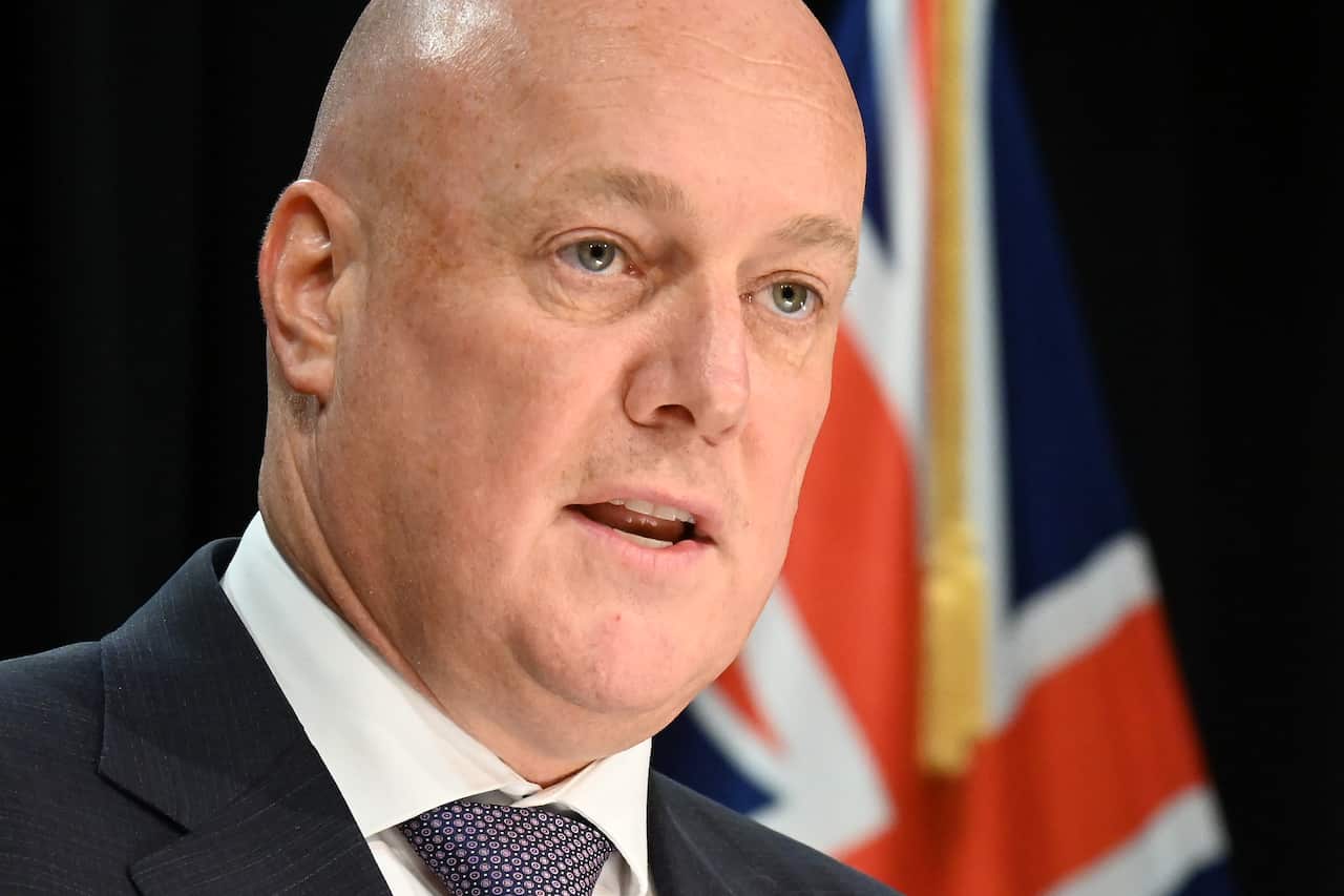 Christopher Luxon speaking in front of a New Zealand flag.