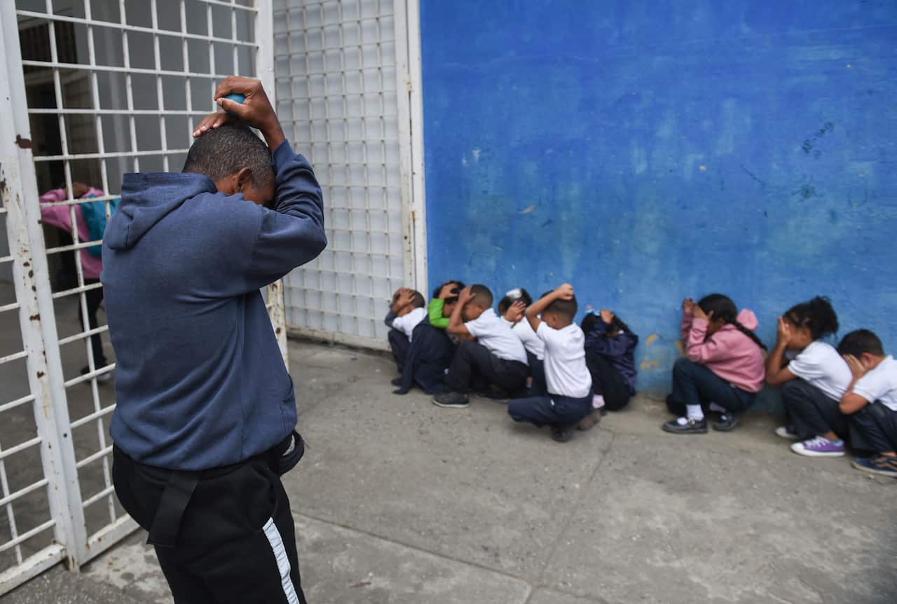 A student standing with his hands on his head, while others crouch with their hands on their heads.