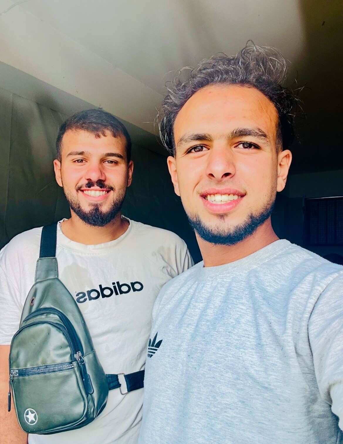 Two young men in T-shirts smile as one takes a selfie-style photo.