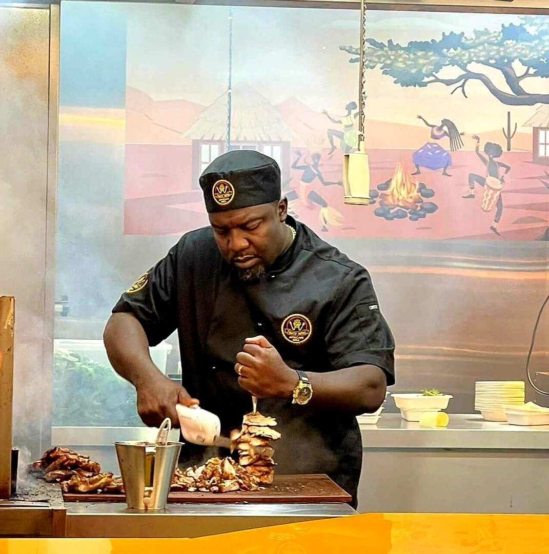 A man in a black chef's uniform shreds cooked meat on a wooden cutting board.