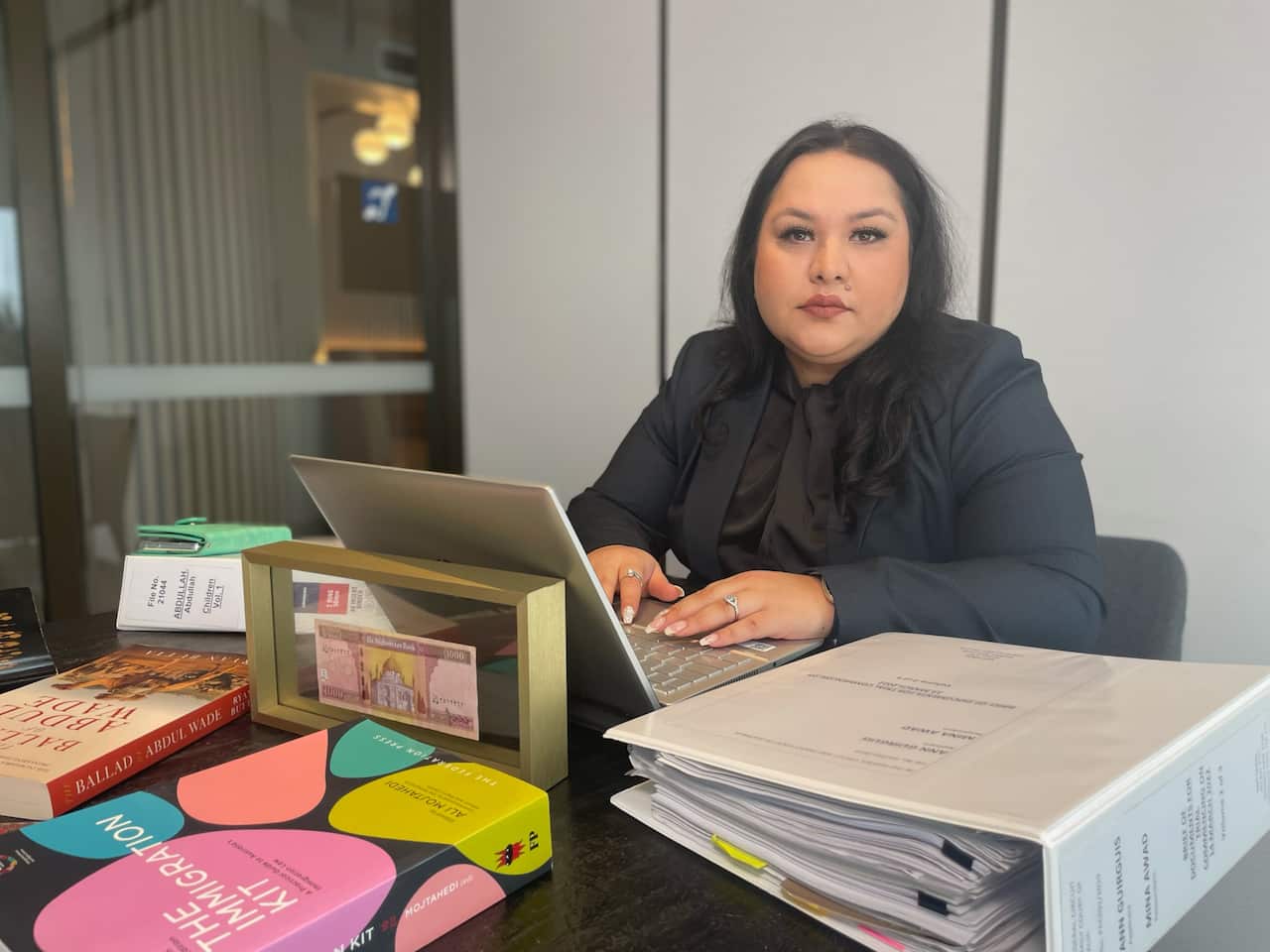 Woman sits at desk in front of laptop and documents.