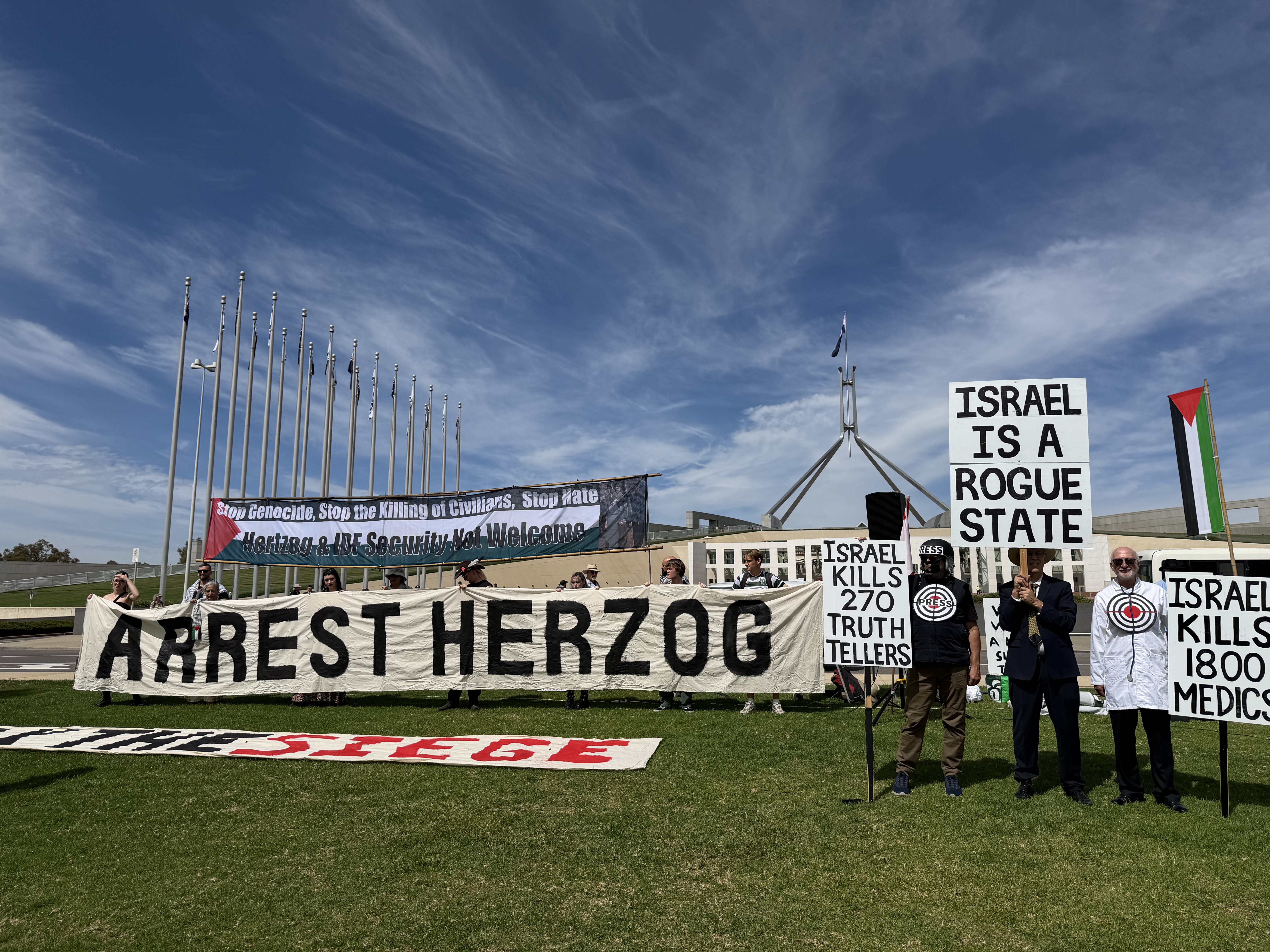 People holding up "arrest Herzog" and anti-Israel banners on the laws of parliament.