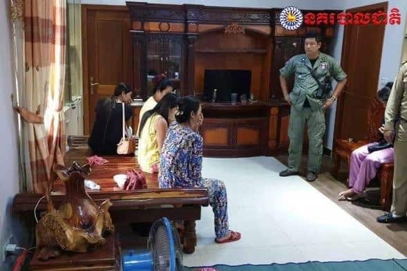 Inside a furnished room, a man in a police uniform standing opposite four crying women seated on a wooden bench