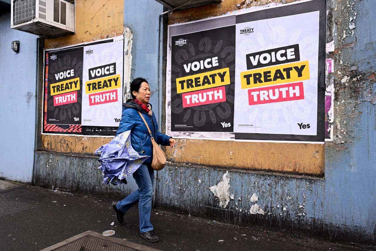 A woman with a bag and umbrella walks past posters on a wall.