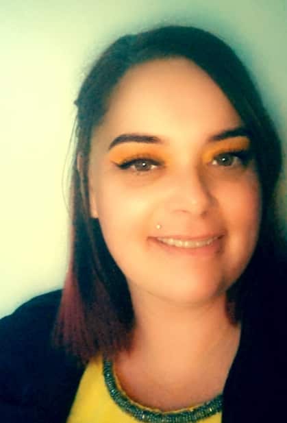 A woman with a lip piercing and dark hair smiles.